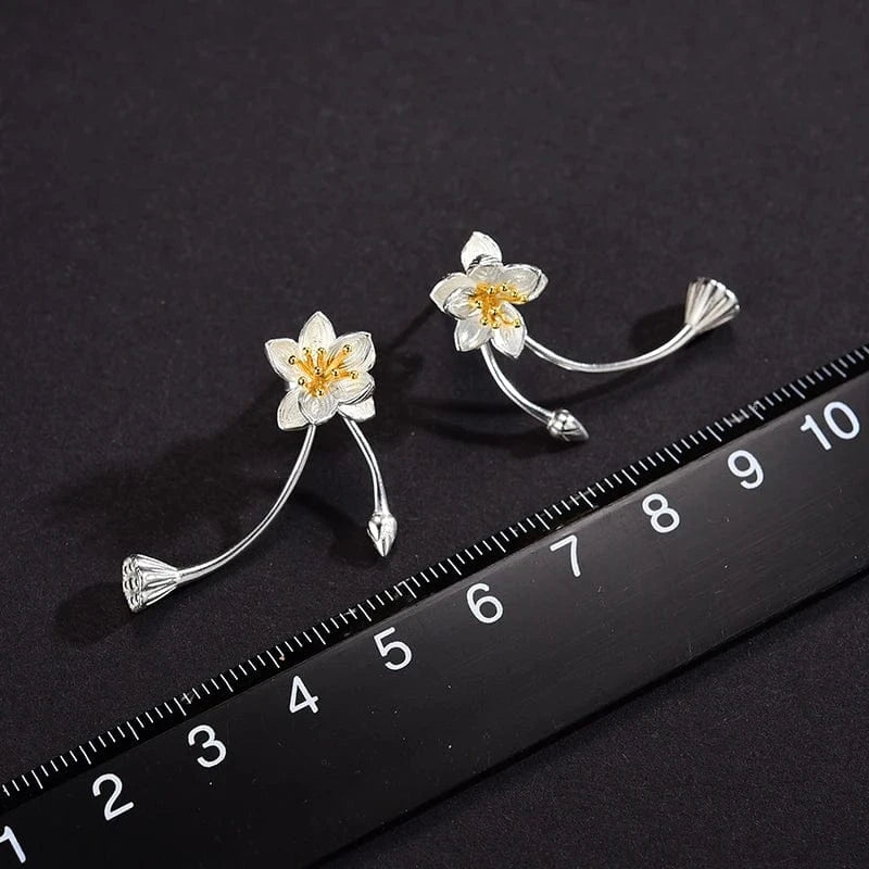 Floral silver earrings on a black background with a ruler for scale.