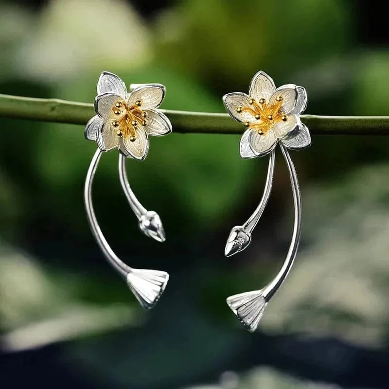 Silver flower-shaped earrings on a branch with a green leafy background