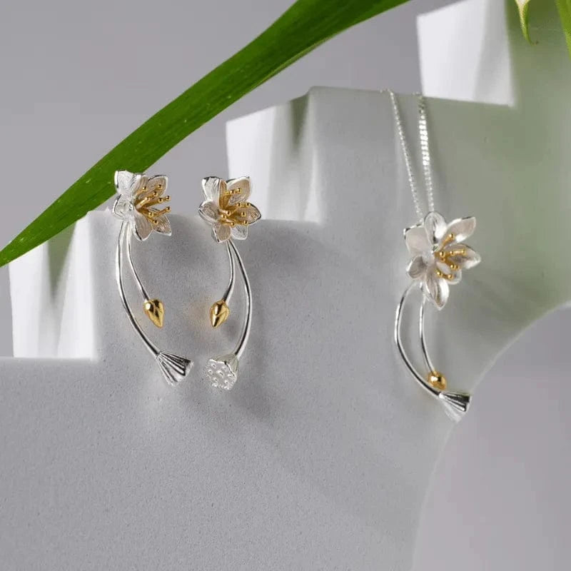 Silver and gold floral earrings on a white surface with a green leaf