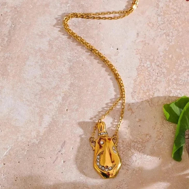 Gold necklace with a lyre-shaped pendant on a textured beige surface.