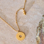 Gold necklace with a unique pendant on a textured stone surface
