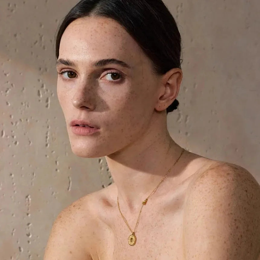 Woman wearing a gold necklace against a neutral background
