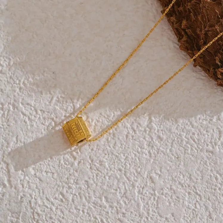 Gold necklace with a square pendant on a textured white surface.
