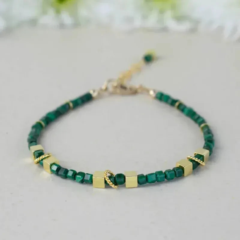 Green beaded bracelet with gold accents on a light gray background