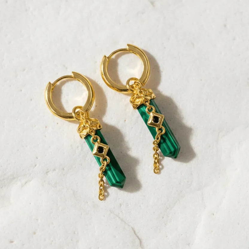 Gold hoop earrings with green gemstone drops on a light background