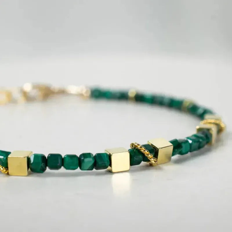 Green beaded bracelet with gold accents on a light gray background
