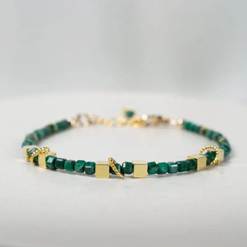 Green beaded bracelet with gold accents on a light gray background