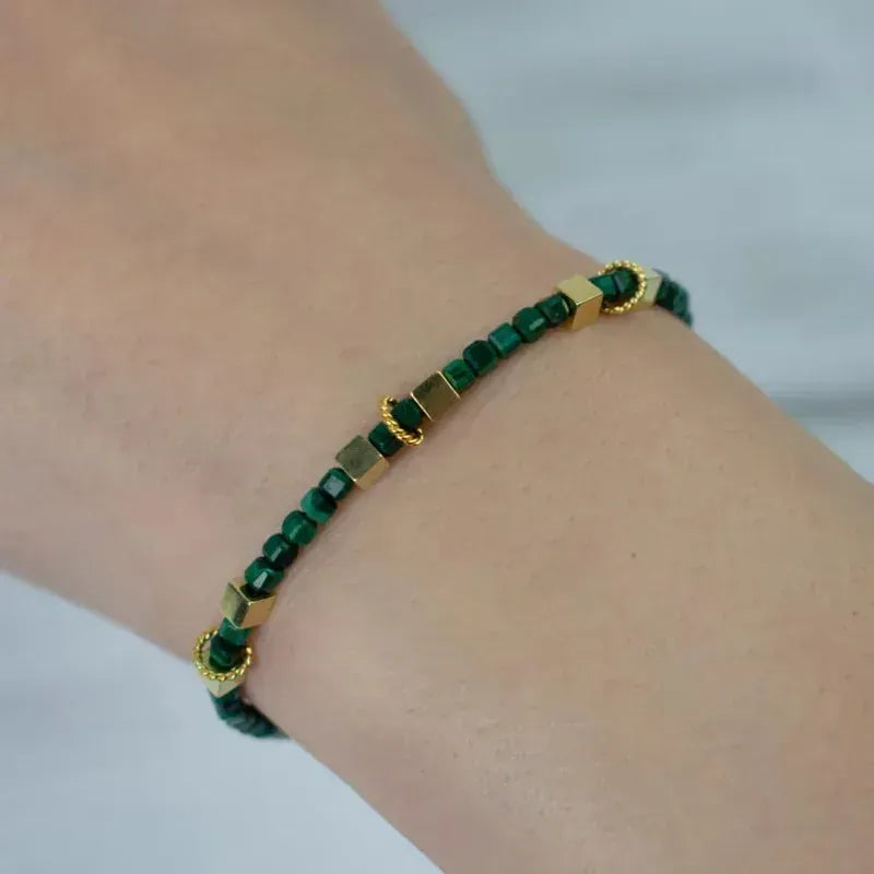 Green beaded bracelet with gold accents on a wrist against a white background