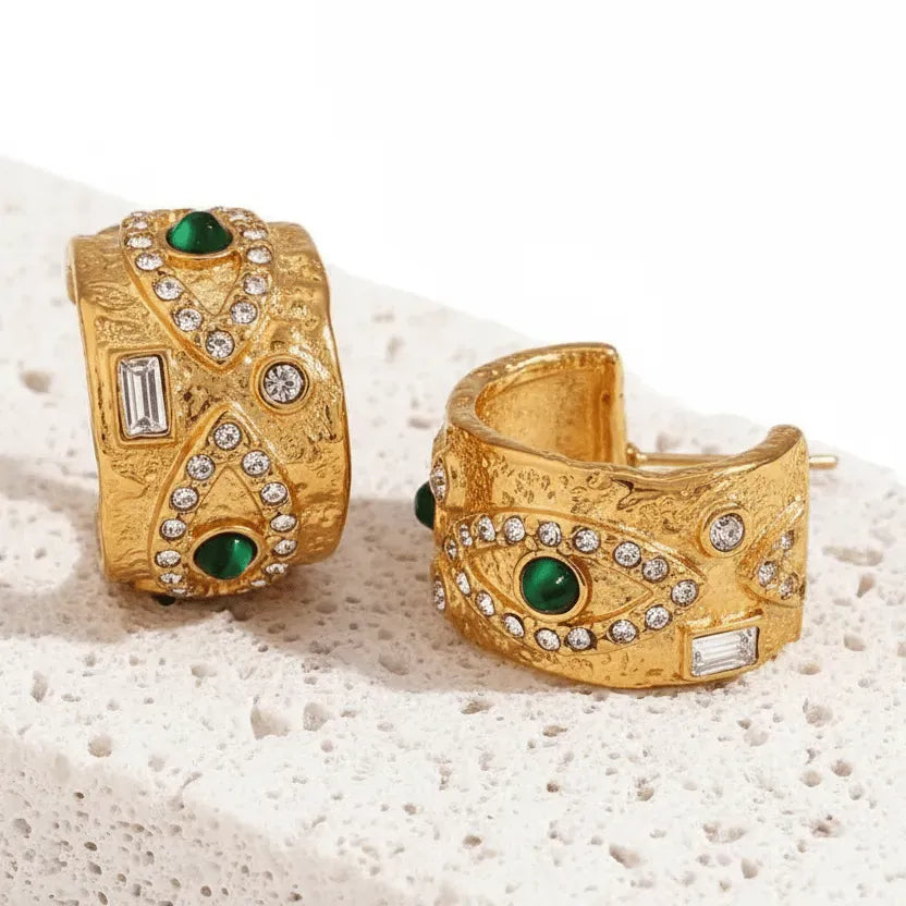 Gold cuff bracelets with green gemstones and rhinestones on a textured surface