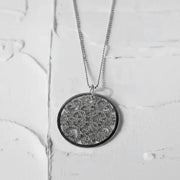 Gold necklace with a detailed pendant on a textured white surface