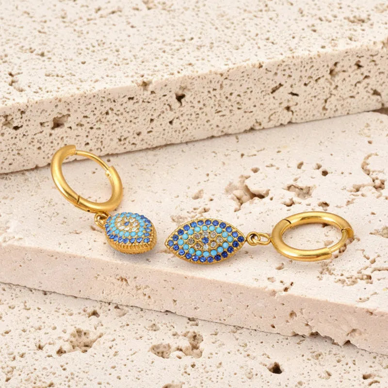 Gold earrings with blue gemstones on a stone surface with yellow flowers.
