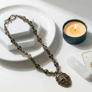 Necklace with a mask pendant next to a lit candle on a white surface