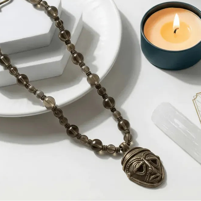 Necklace with a mask pendant next to a lit candle on a white surface
