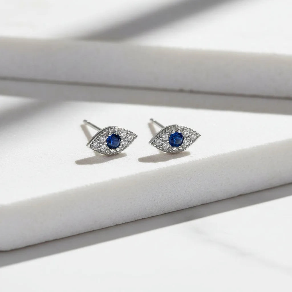 Pair of silver eye-shaped earrings with blue gemstones on a white background,