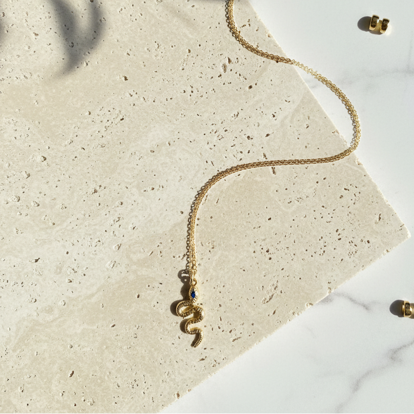 Gold snake necklace with a blue eye, flat lay — spirit animal jewelry for transformation