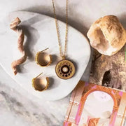 Gold necklace and earrings on a marble surface with decorative elements.