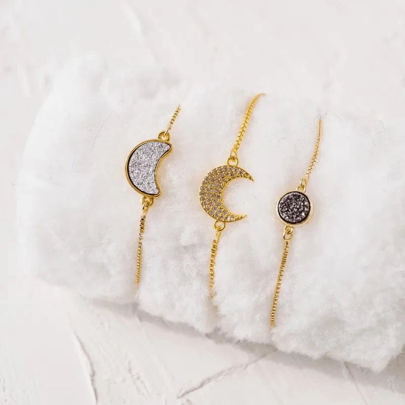 Two gold moon-shaped earrings with gemstone details on a white fur surface.