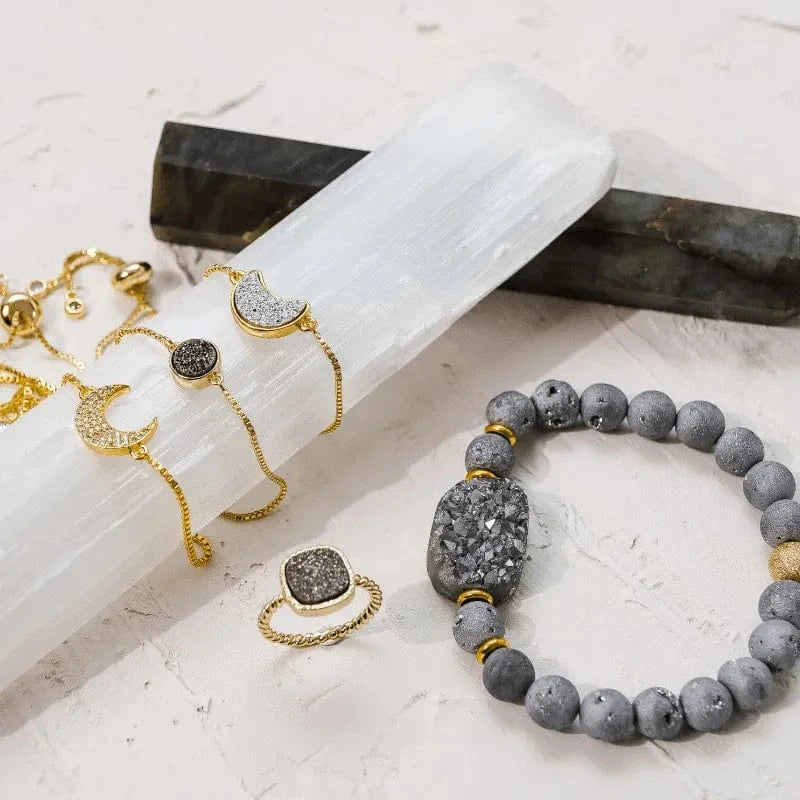 Gray beaded bracelet with gold accents on a white surface with other jewelry items.