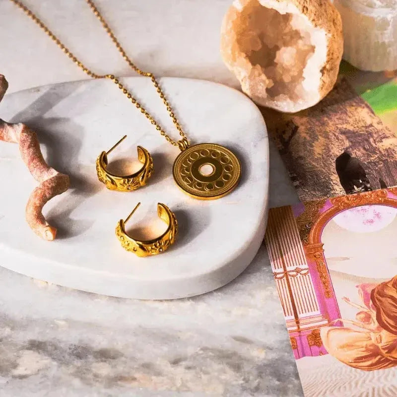 Gold jewelry set including necklace and earrings on a marble surface with crystals and cards.
