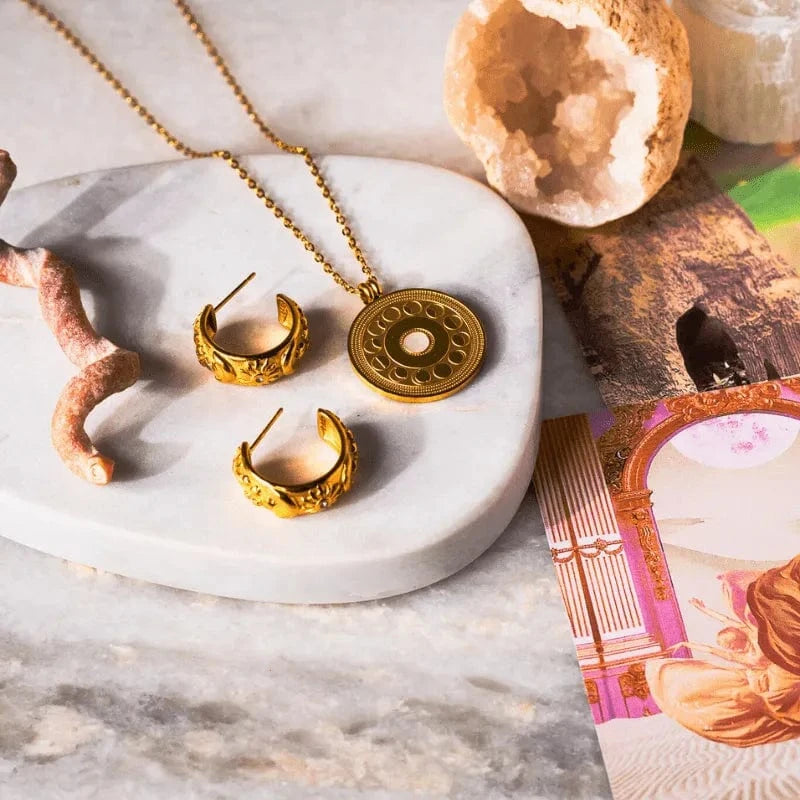 Gold jewelry set including necklace and earrings on a marble surface with crystals and cards.