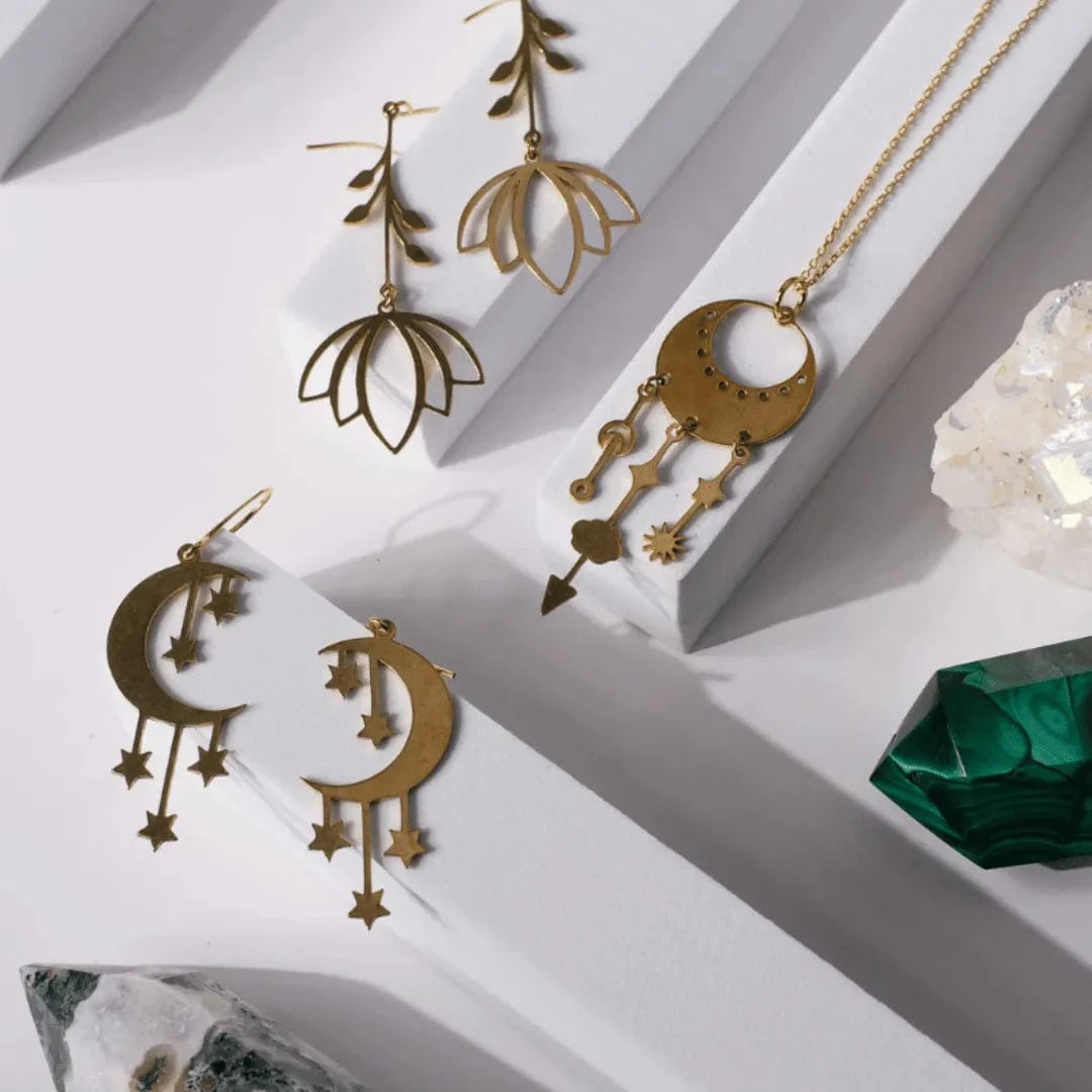 Gold jewelry set including earrings and a necklace on a white surface with geometric shadows.