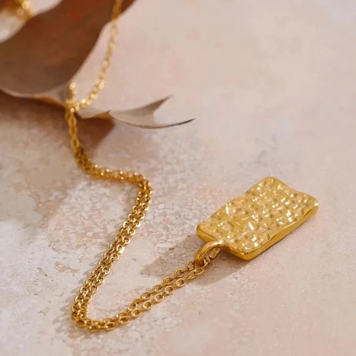 Gold necklace with a textured pendant on a light background