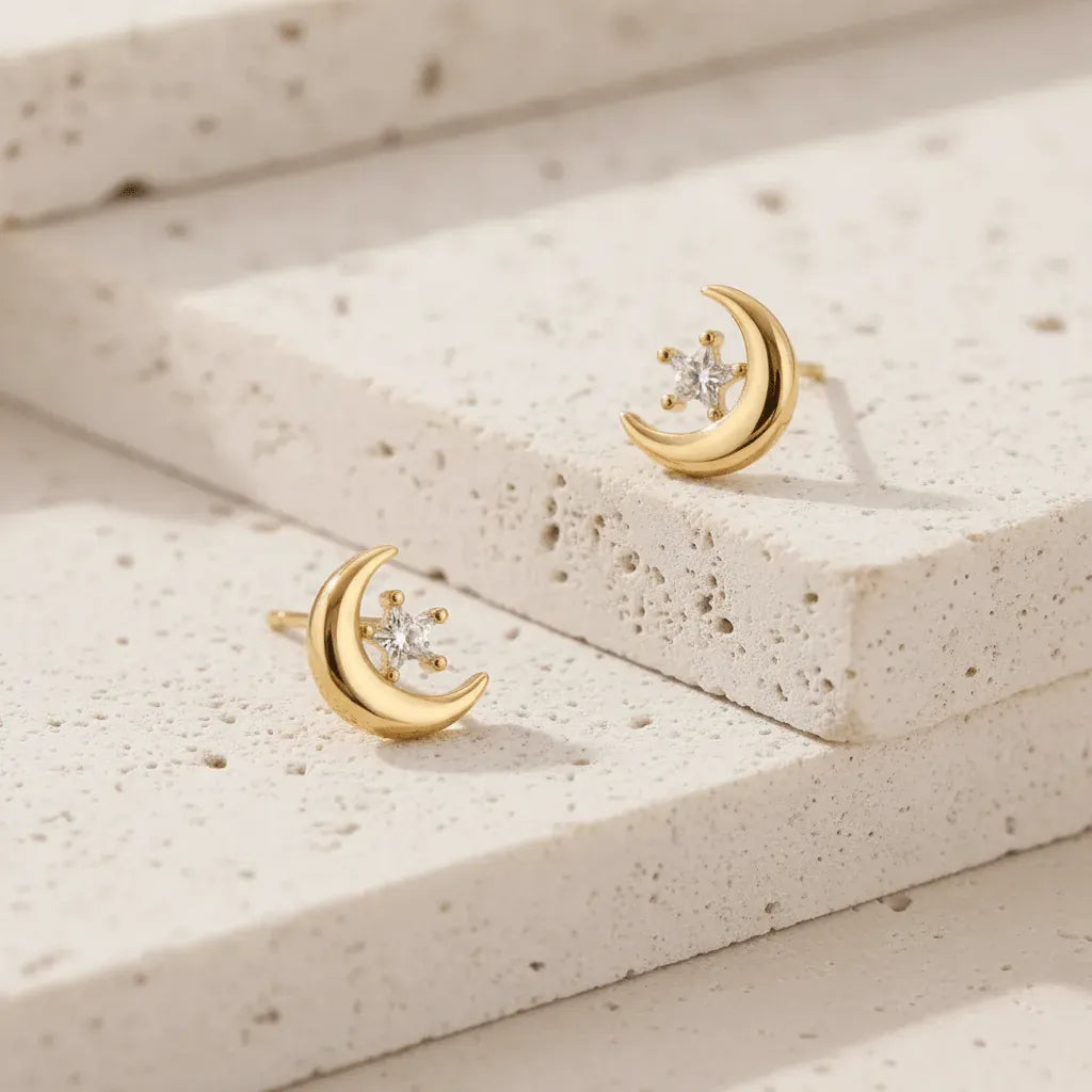 Gold moon-shaped earrings with embedded diamonds on a textured beige surface