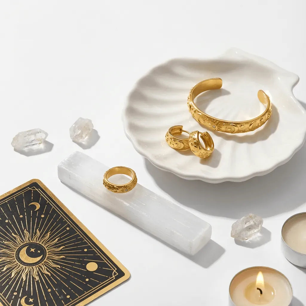 Gold jewelry including a bracelet and rings on a white surface with crystals and a candle.