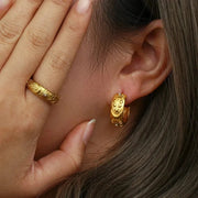 Close-up of a person wearing gold hoop earrings and a matching ring.