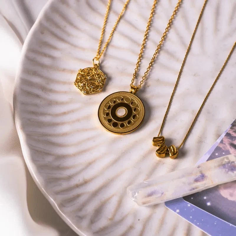 Three gold necklaces with unique pendants on a textured ceramic plate.