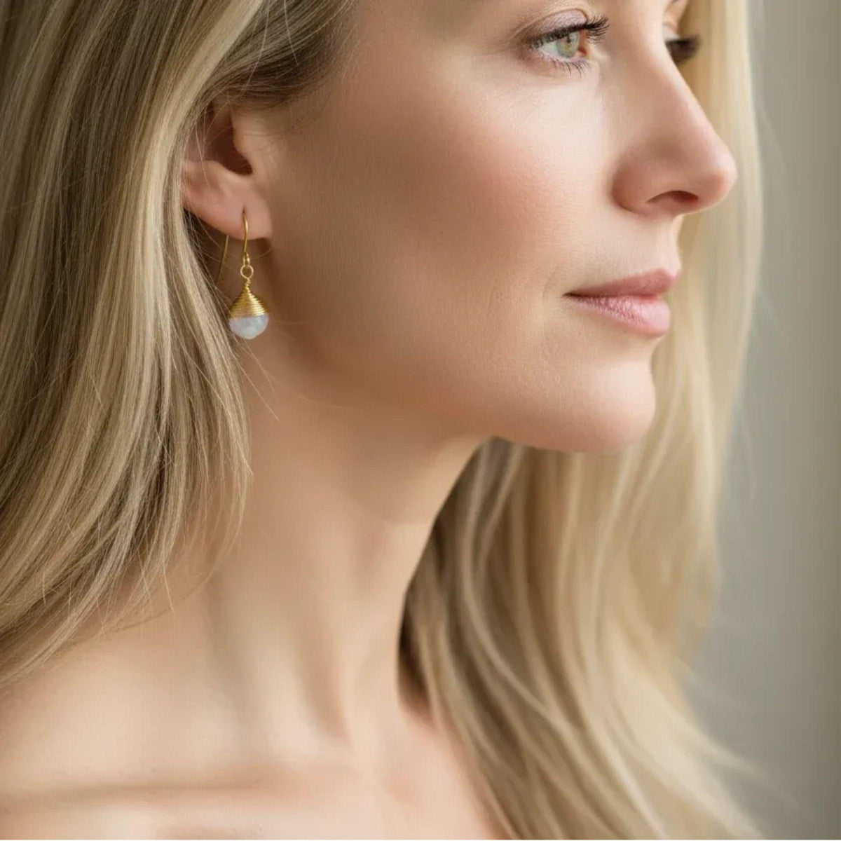 Woman wearing faceted moonstone drop earrings wrapped in gold wire