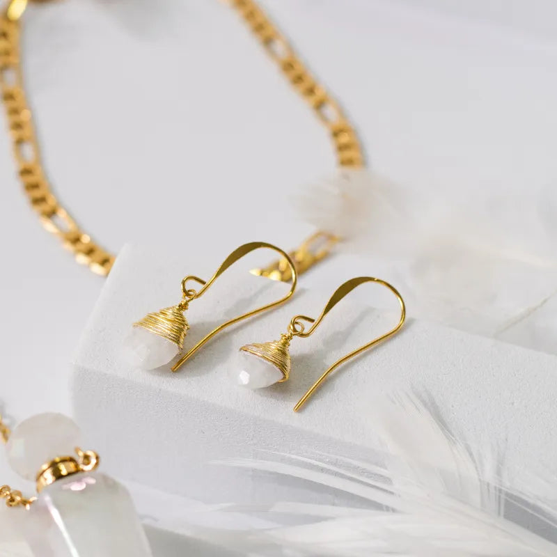 Gold earrings with white stones on a soft white background