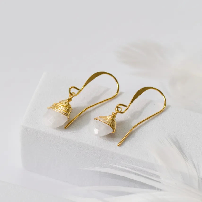 Gold earrings with white beads on a light fabric background