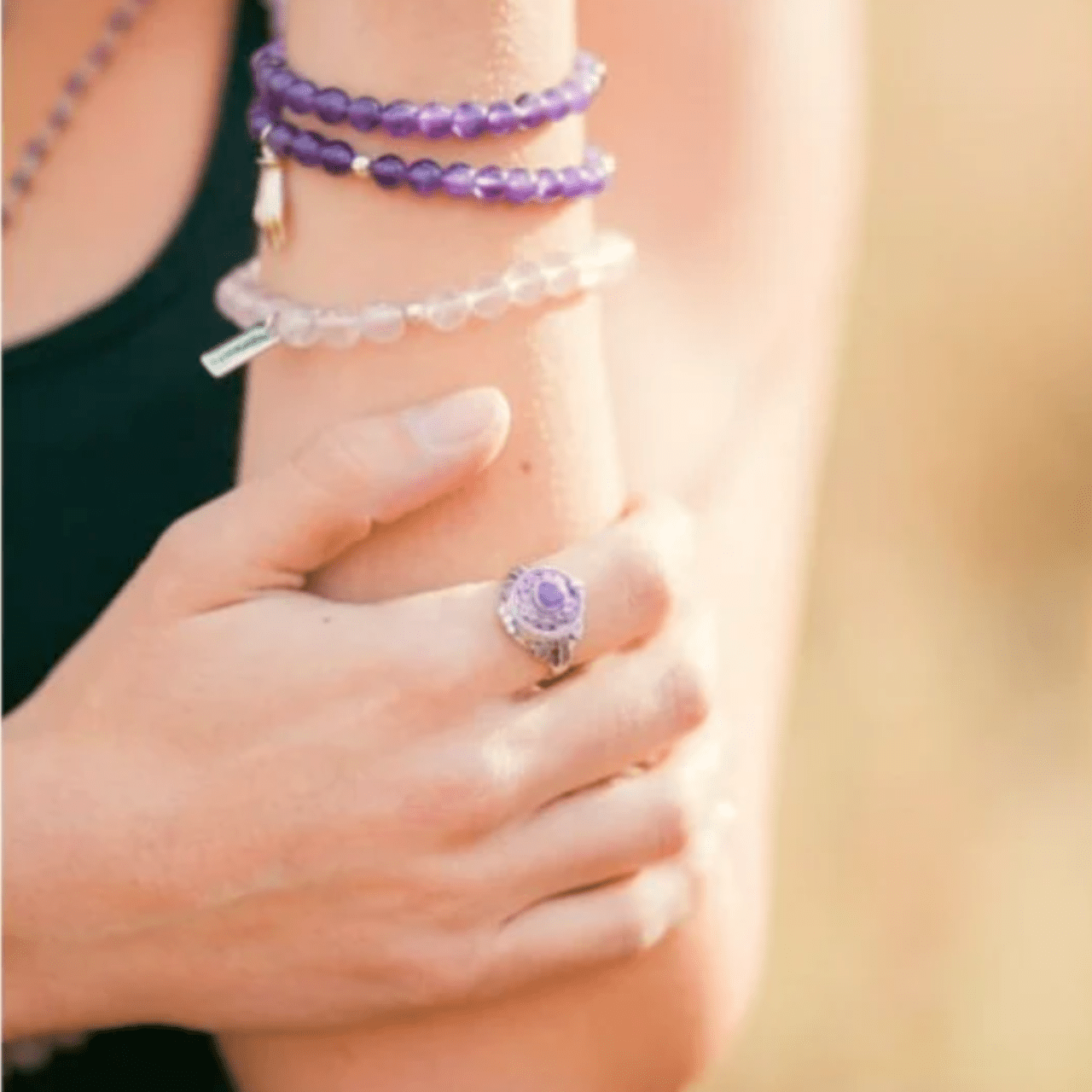 Close-up of a person wearing a purple ring and bracelets on a blurred background