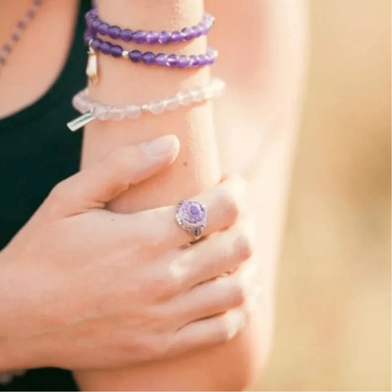 Close-up of a person wearing a purple ring and bracelets on a blurred background
