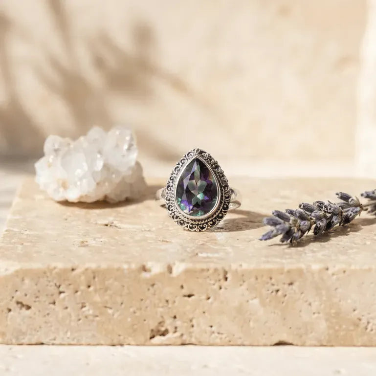 Ring with teardrop-shaped gemstone on a stone surface with a blurred natural background