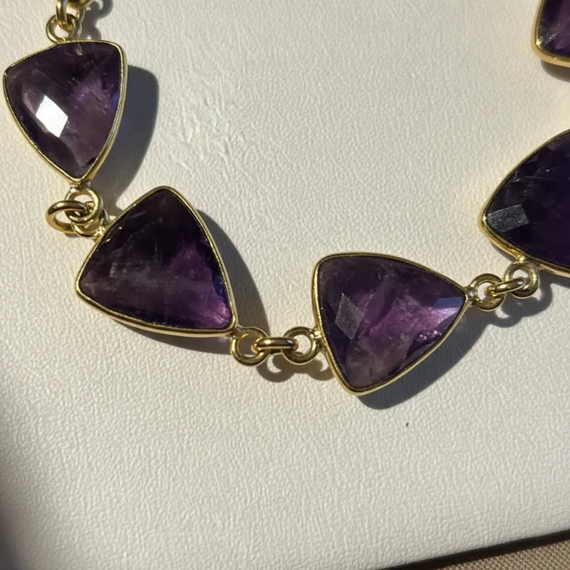 Close-up of faceted shield-cut natural amethyst stones on a gold-plated chain necklace