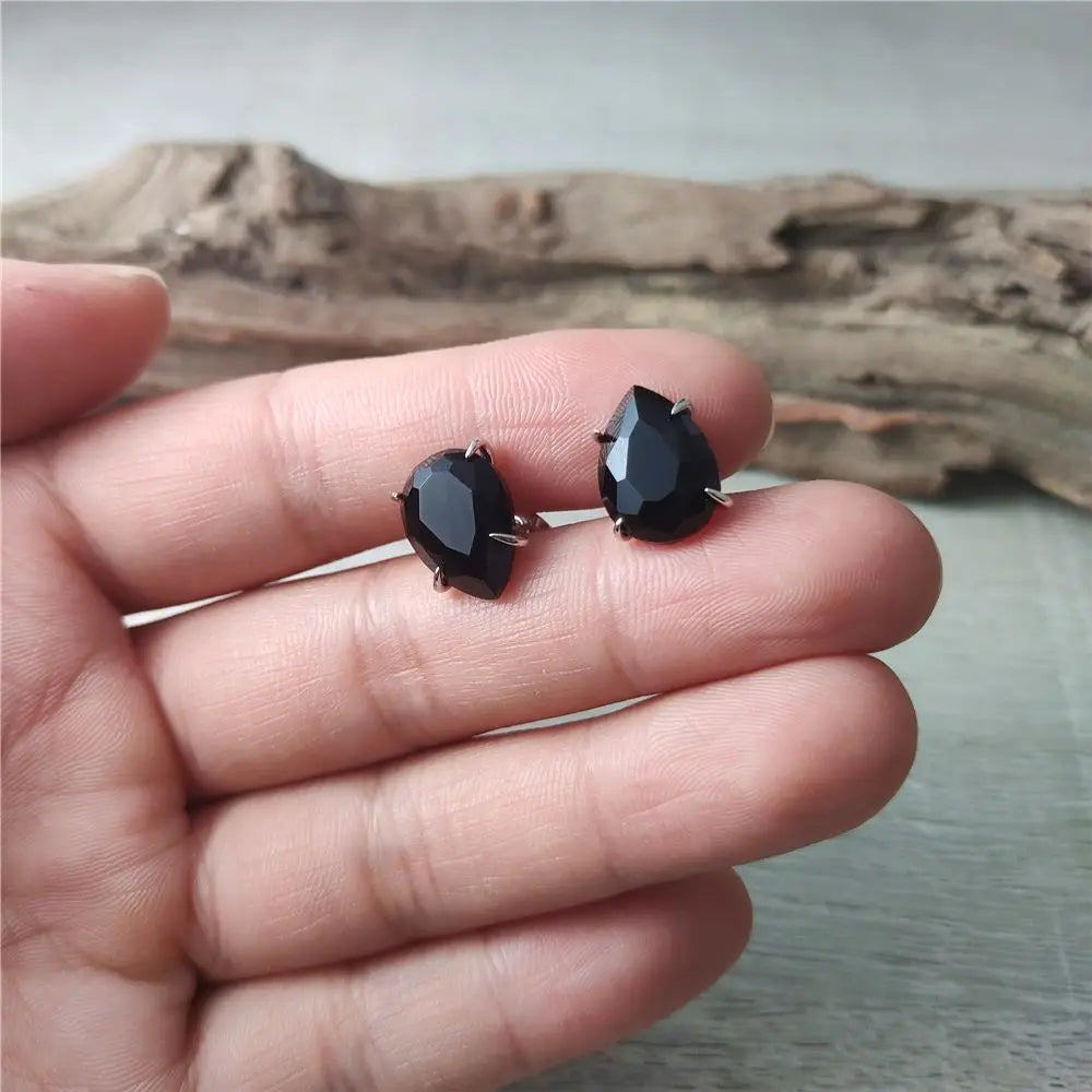 Black teardrop-shaped earrings held between fingers with a natural wood background