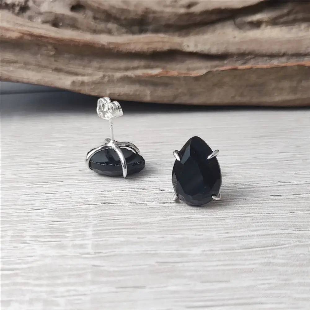 Black teardrop earrings with silver posts on a light gray surface.