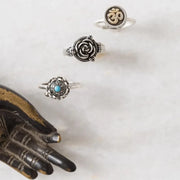 Three silver rings with intricate designs on a marble surface next to a bronze hand sculpture.