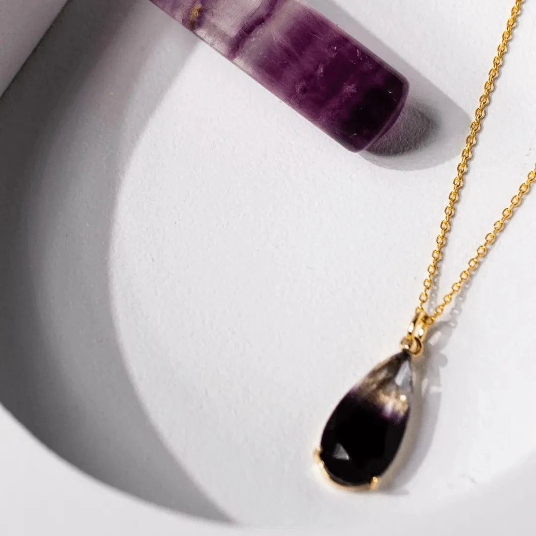 Necklace with a purple teardrop pendant and gold chain on a white background