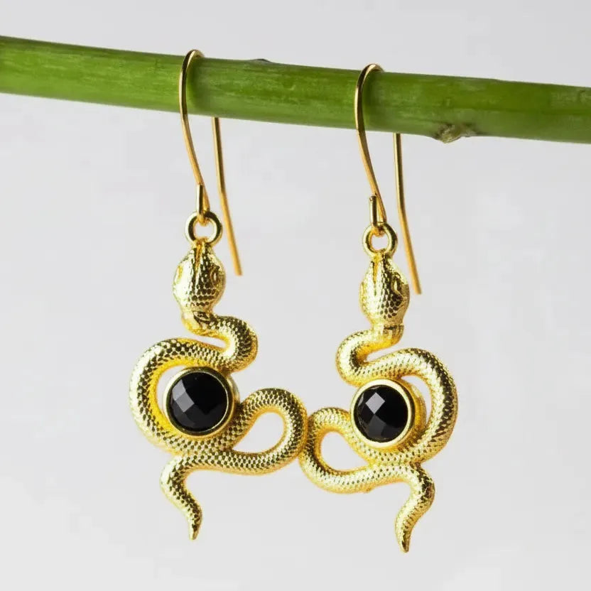 Gold snake-shaped earrings with black stones on a white background