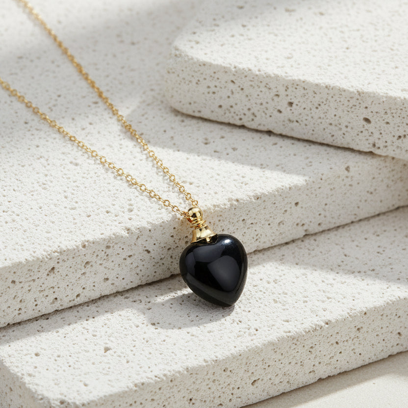 Gold necklace with a black heart-shaped pendant on a white background