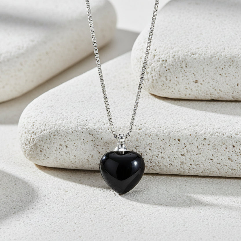 Black heart-shaped pendant on a silver chain against a white background