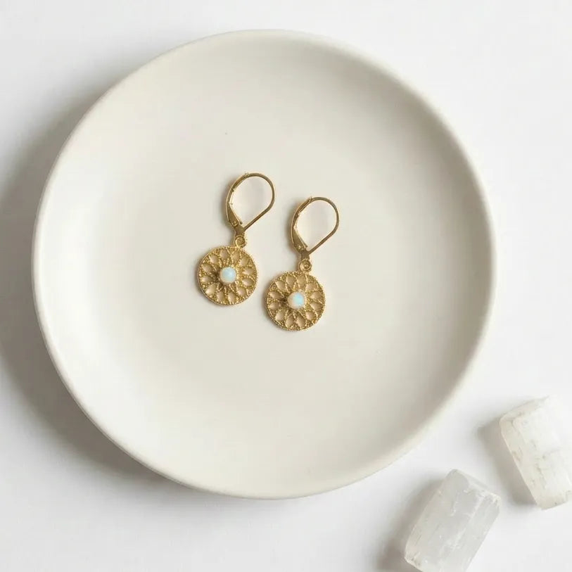 Gold earrings on a white plate with crystals on a light gray background