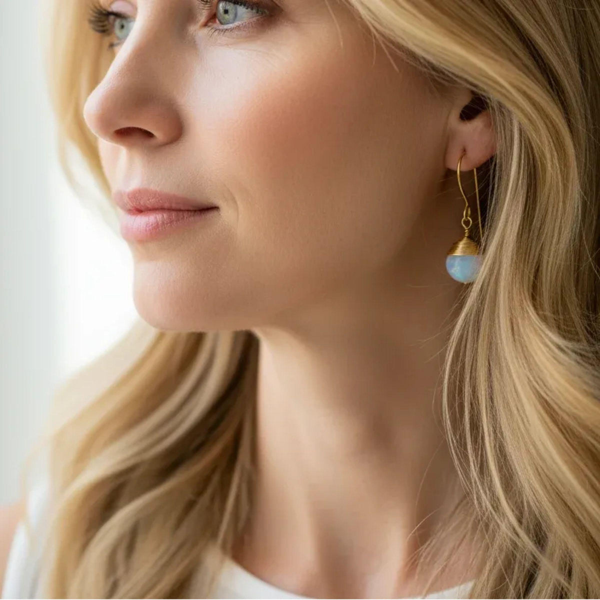 Woman wearing faceted opalite drop earrings wrapped in gold wire, milky blue-lavender glass