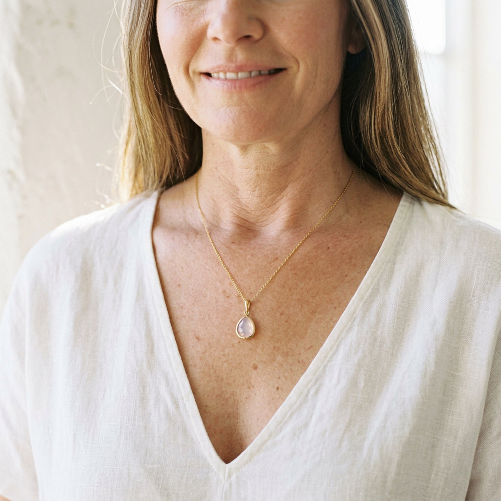 Woman wearing a gold teardrop necklace with iridescent opalite glass pendant, opal-inspired October colour