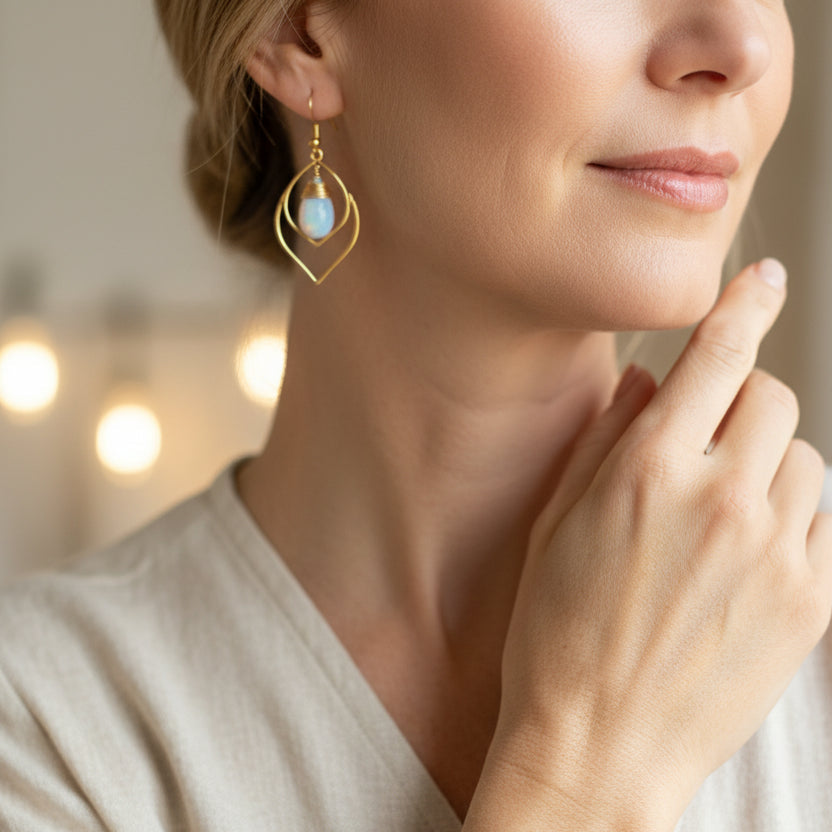 Gold earrings with opal stones on a white surface with colorful stones in the background