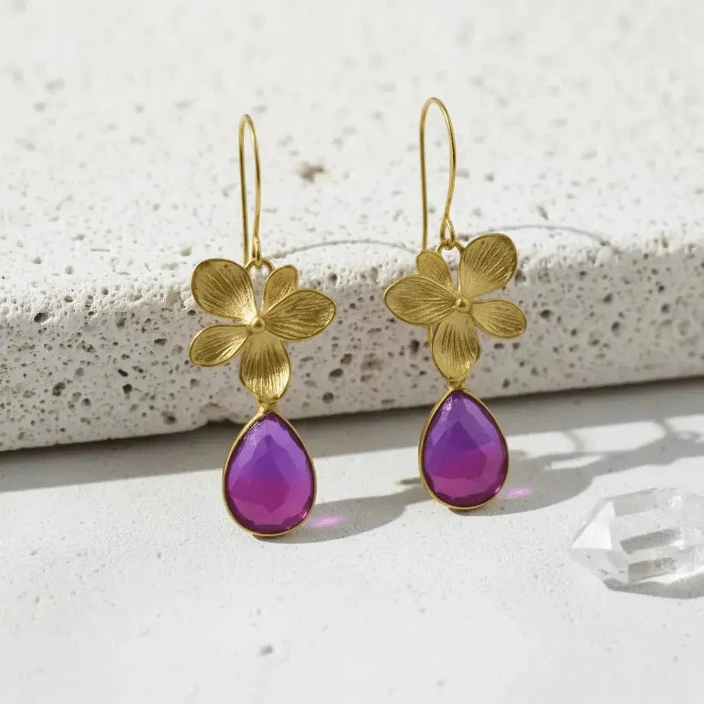 Gold flower earrings with purple teardrop stones on a light background