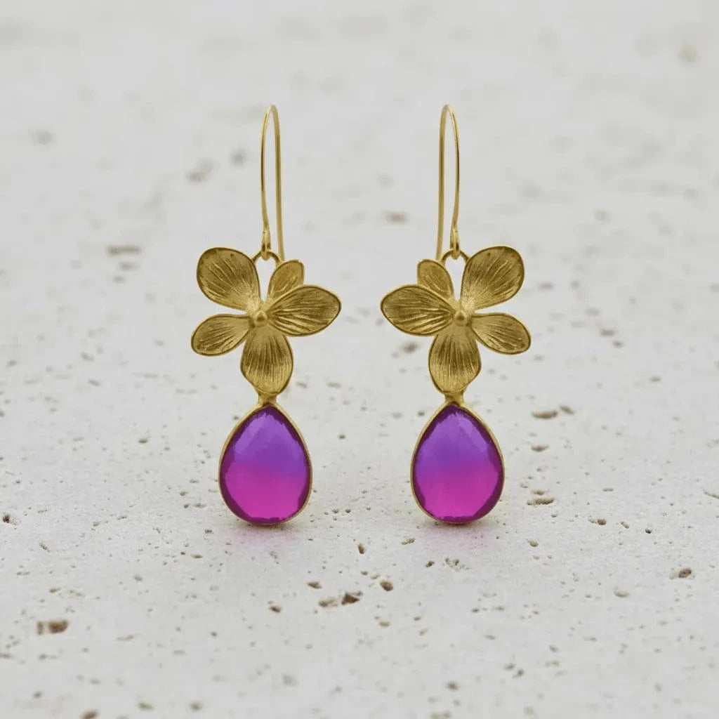 Gold flower earrings with purple teardrop stones on a light background